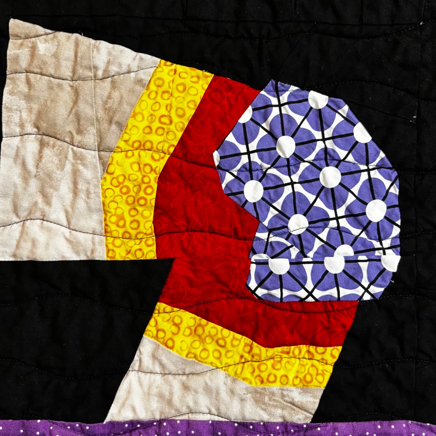 Abstract pieced block in red, yellow, and purple prints on black fabric